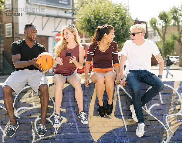 Männliche und weibliche Basketballfreunde sitzen im städtischen Skatepark und unterhalten sich