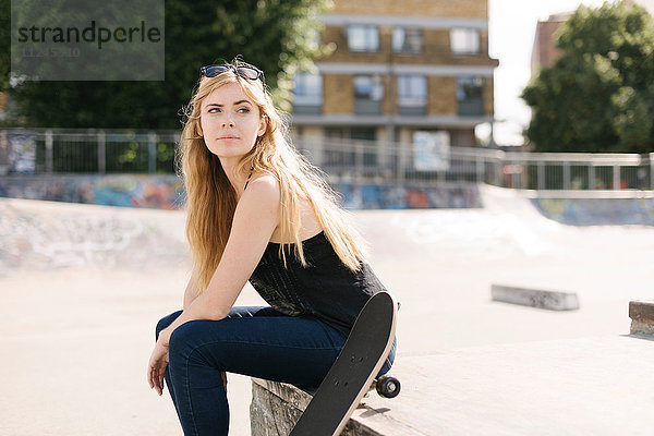Porträt einer jungen Skateboarderin im Skatepark sitzend