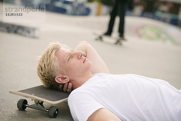 Junger männlicher Skateboarder mit geschlossenen Augen im Skatepark liegend