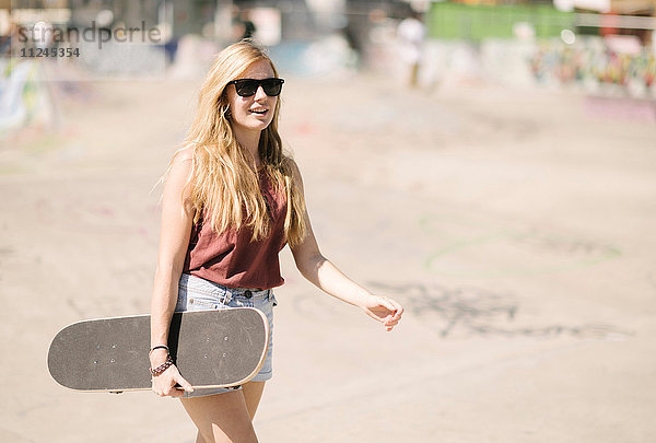 Junge Frau geht mit Skateboard im Skatepark