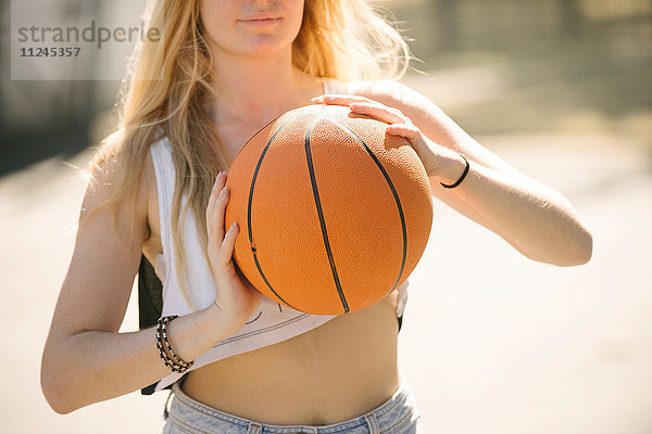 Mittlere Sektion einer jungen Frau beim Training auf dem Basketballplatz