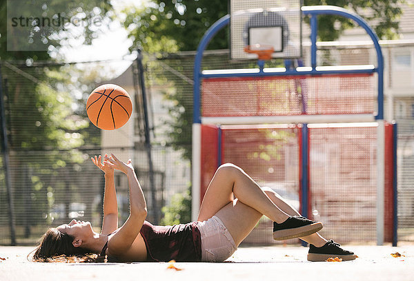 Junge Frau liegt auf Basketballfeld und wirft Ball