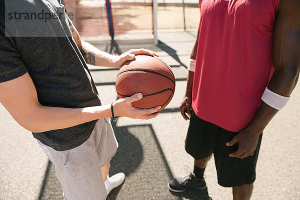 Mittelteil von zwei männlichen Basketballspielern mit Ball auf dem Basketballfeld