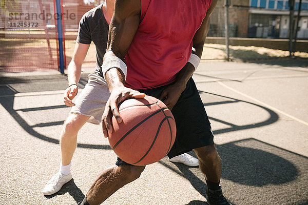 Mittelteil von zwei männlichen Basketballspielern beim Training auf dem Basketballplatz