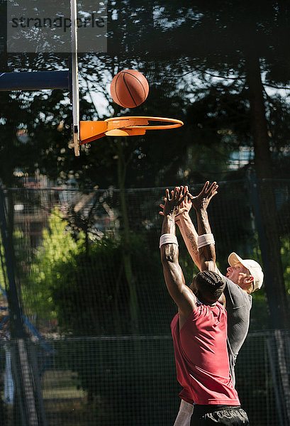 Junge männliche Basketballspieler werfen Ball auf Basketballkorb