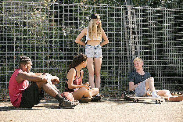 Vier erwachsene Skateboarder-Freunde sitzen plaudernd auf dem Basketballplatz