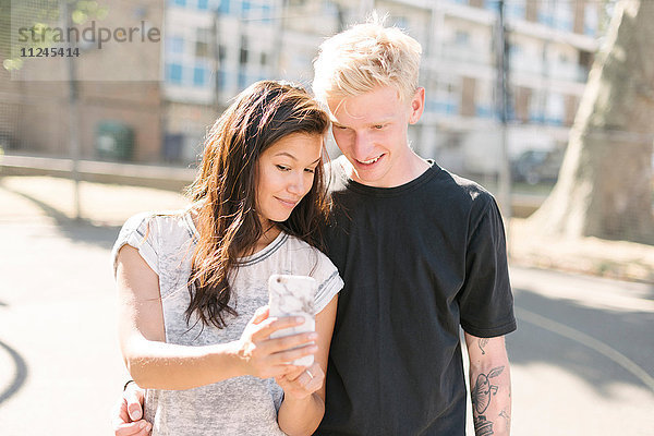 Frau und Freund lesen Smartphone-Update auf dem Basketballplatz