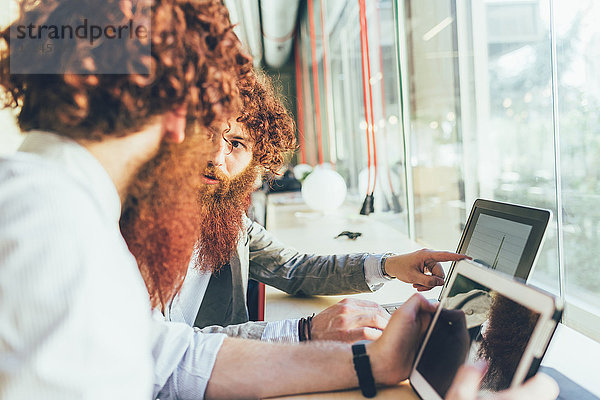 Männliche erwachsene Hipster-Zwillinge zeigen im Büro auf einen Laptop