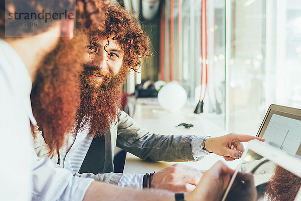 Männliche erwachsene Hipster-Zwillinge zeigen im Büro auf einen Laptop