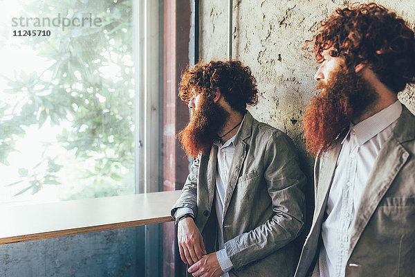 Eineiige männliche Hipster-Zwillinge  die aus dem Bürofenster schauen.