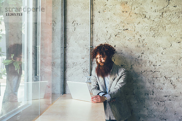 Junger männlicher Hipster mit lockigen roten Haaren und Bart am Laptop im Büro