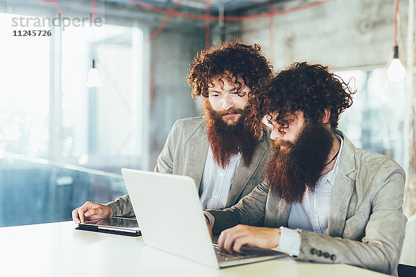 Männliche Hipster-Zwillinge bei der Arbeit am Laptop am Schreibtisch