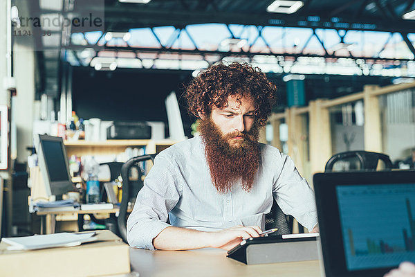 Junger männlicher Hipster mit digitalem Tablett am Schreibtisch