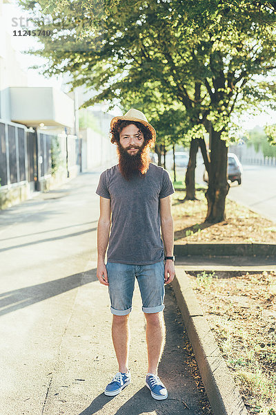Porträt eines jungen männlichen Hipsters mit Strohhut auf dem Bürgersteig