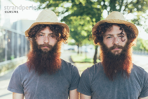 Porträt von eineiigen männlichen Hipster-Zwillingen mit Strohhut auf dem Bürgersteig