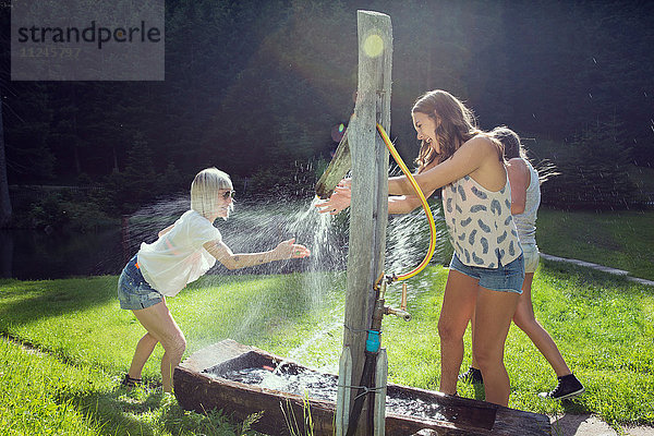 Drei erwachsene Freundinnen spielen im Garten gegen den Sprühwasserschlauch