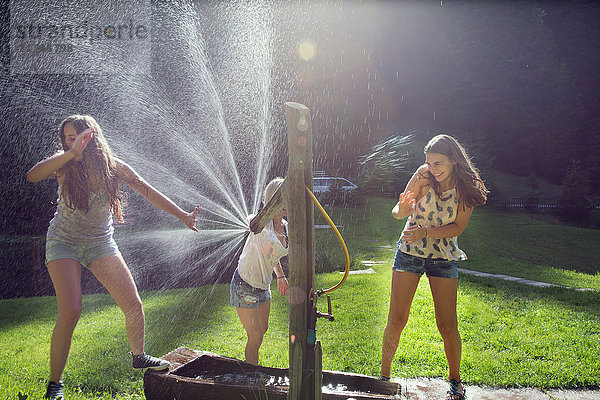Drei erwachsene Freundinnen spielen im Garten gegen den Sprühwasserschlauch