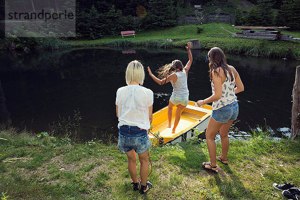 Drei erwachsene Freundinnen springen auf dem See in ein Ruderboot  Sattelbergalm  Tirol  Österreich