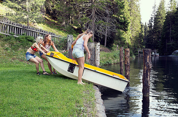Drei erwachsene Freundinnen lassen Ruderboot in den See gleiten  Sattelbergalm  Tirol  Österreich