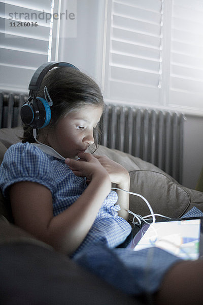 Schulmädchen sitzt auf dem Sofa mit einem digitalen Tablet und hört Kopfhörer