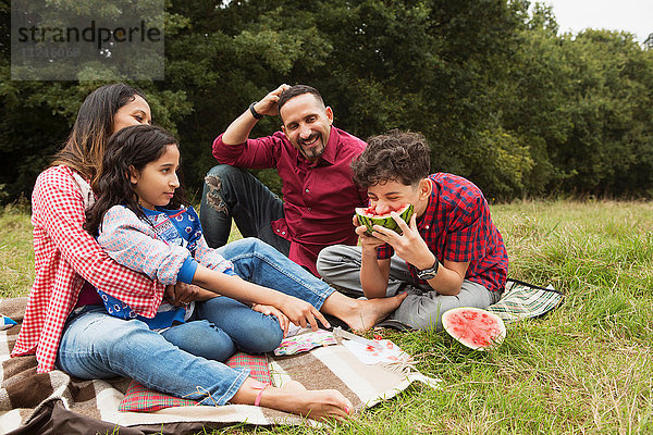 Familie sitzt im Freien  auf einer Picknickdecke  Sohn isst Wassermelone