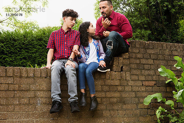 Vater sitzt mit Sohn und Tochter an der Wand