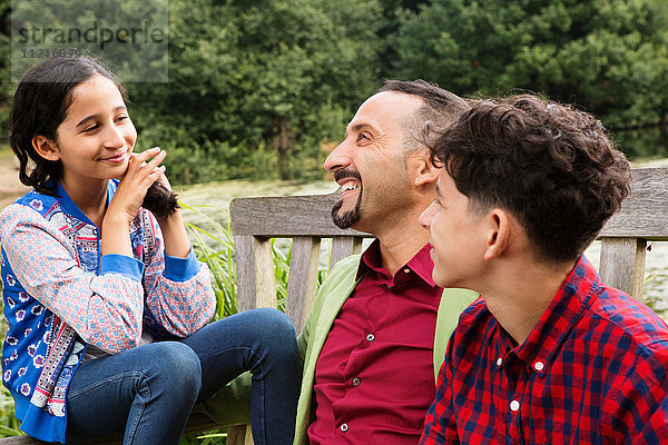 Vater sitzt mit Sohn und Tochter auf der Bank und lacht