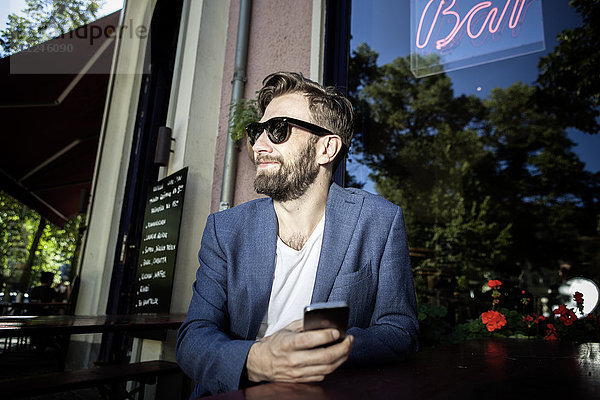 Mann vor der Bar mit lächelndem Smartphone in der Hand  Berlin  Deutschland