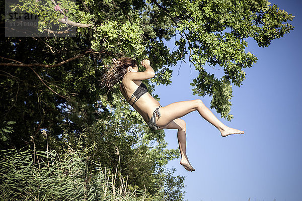 Frau im Bikini auf Baumschaukel schwimmend