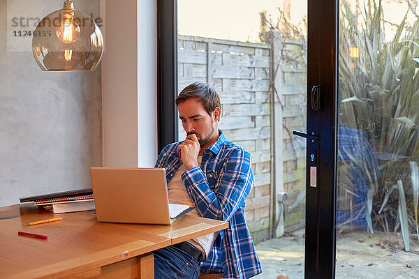 Mid Erwachsene Mann Lesung Laptop-Update am Esstisch