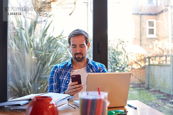 Mittlerer Erwachsener Mann liest Smartphone-Text am Esstisch