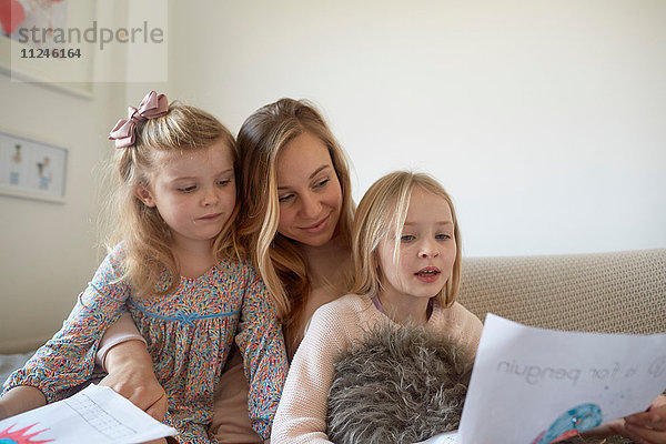 Mittlere erwachsene Frau betrachtet Zeichnungen mit Töchtern im Wohnzimmer