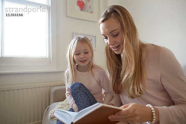 Mittlere erwachsene Frau liest der Tochter im Wohnzimmer vor