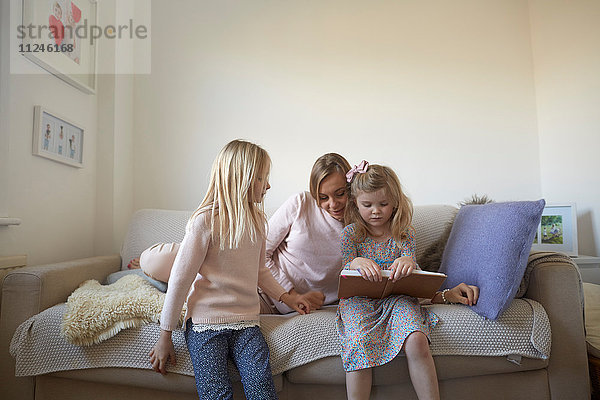 Mittlere erwachsene Frau und Töchter lesen Märchenbuch auf dem Sofa