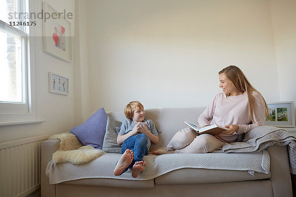 Mittlere erwachsene Frau und Sohn lesen auf dem Sofa ein Märchenbuch
