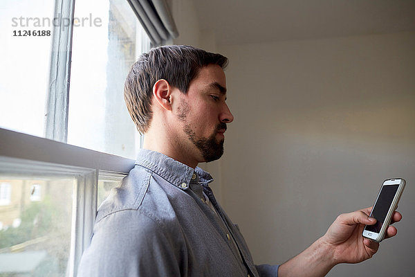 Mid Erwachsene Mann am Fenster lesen Smartphone-Texte