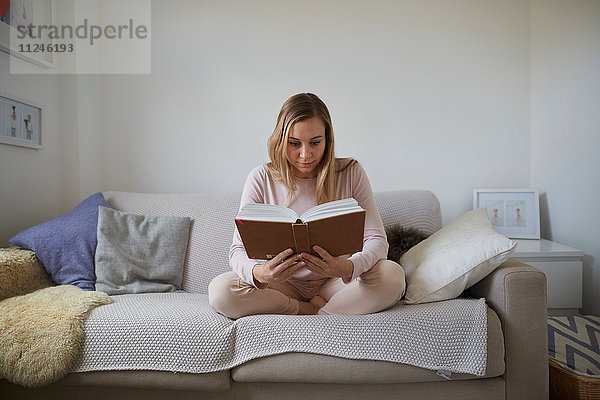 Mittlere erwachsene Frau liest Buch auf Wohnzimmersofa