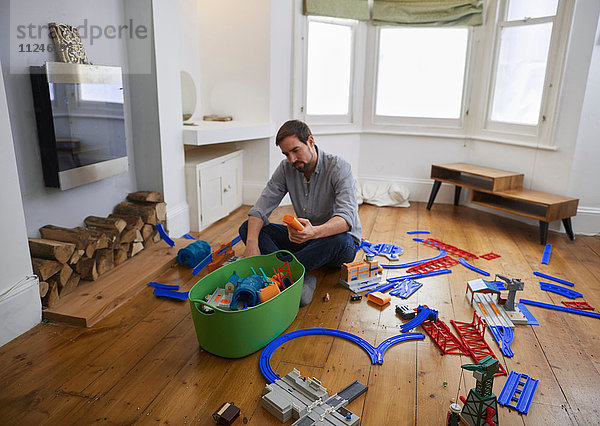 Mittelgroßer erwachsener Mann betrachtet im Wohnzimmer verstreutes Spielzeug