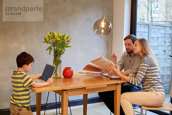 Mittelgroßes erwachsenes Paar  das sich am Esstisch Papierkram ansieht  während der Sohn einen Laptop benutzt