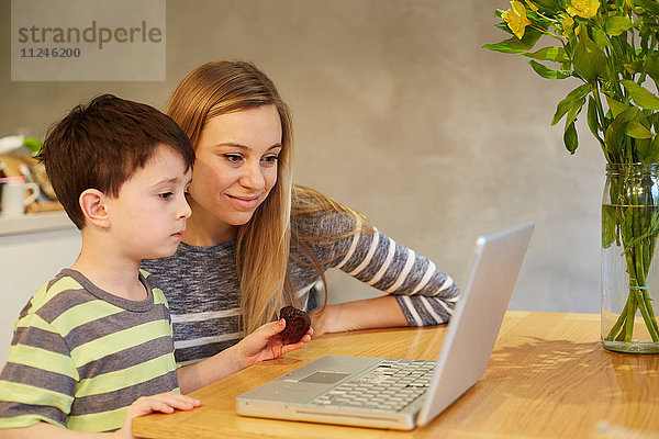 Mittelgroße erwachsene Frau und Sohn schauen auf den Laptop auf dem Esstisch