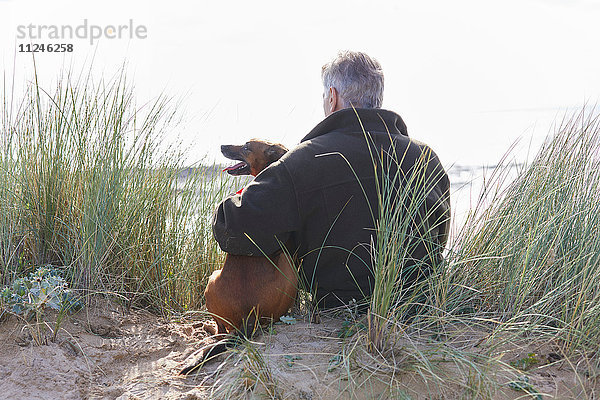 Rückansicht von Mensch und Haushund auf Sanddünen sitzend  Constantine Bay  Cornwall  UK