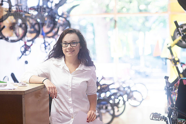 Frau im Fahrradgeschäft lehnt gegen die Ladentheke und schaut lächelnd in die Kamera