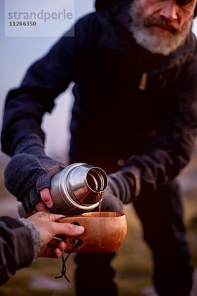 Wanderer schüttet Kaffee in die Tasse eines Freundes