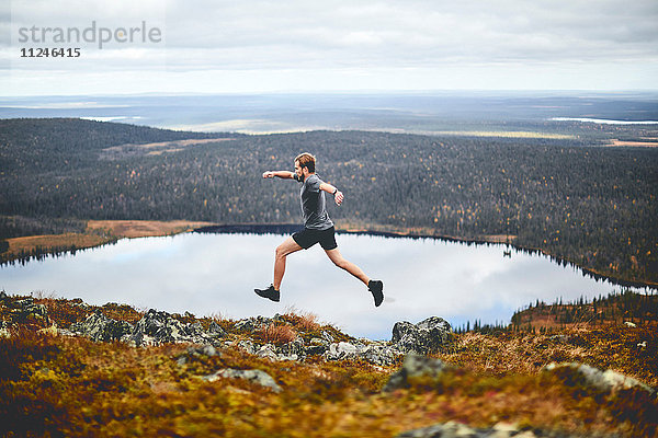 Mann sprintet auf felsigem Klippengipfel  Keimiotunturi  Lappland  Finnland