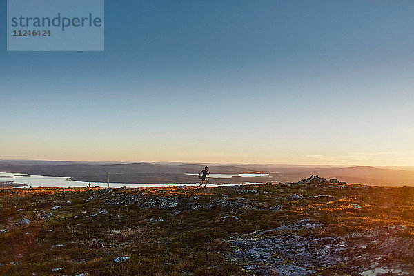 Mann rennt bei Sonnenuntergang auf den Klippen  Keimiotunturi  Lappland  Finnland