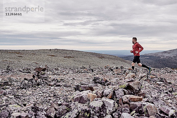Mann läuft auf felsiger Felsspitze  Kesankitunturi  Lappland  Finnland
