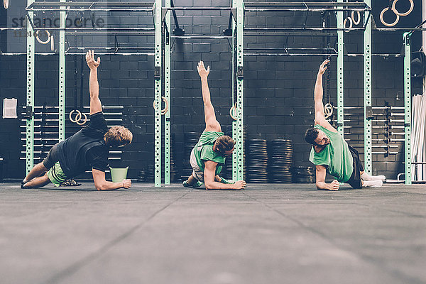 Drei männliche Crosstrainer machen seitliche Liegestütze im Fitnessstudio