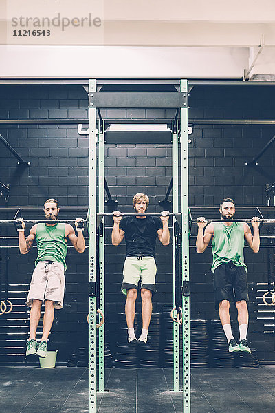 Zwei männliche Crosstrainer machen im Fitnessstudio Kinnübungen an der Übungsstange