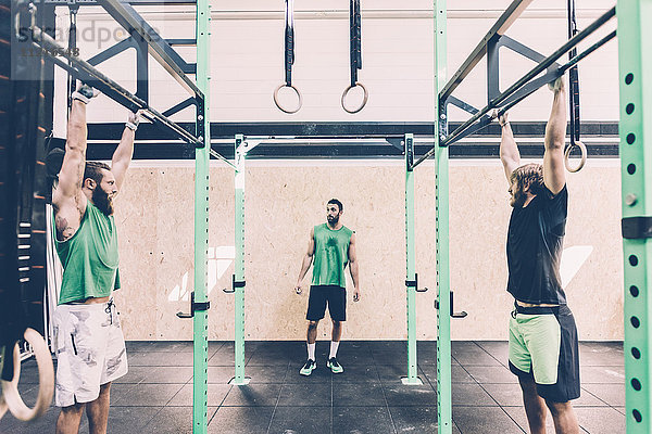 Zwei männliche Crosstrainer trainieren im Fitnessstudio an der Stange