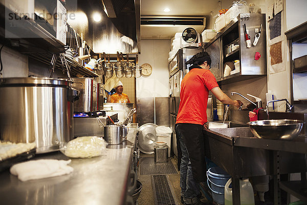 Der Ramen-Nudel-Laden. Ein Küchenchef  der in einer Küche arbeitet  in der das Essen mit einem Herd und großen Pfannen zubereitet wird.